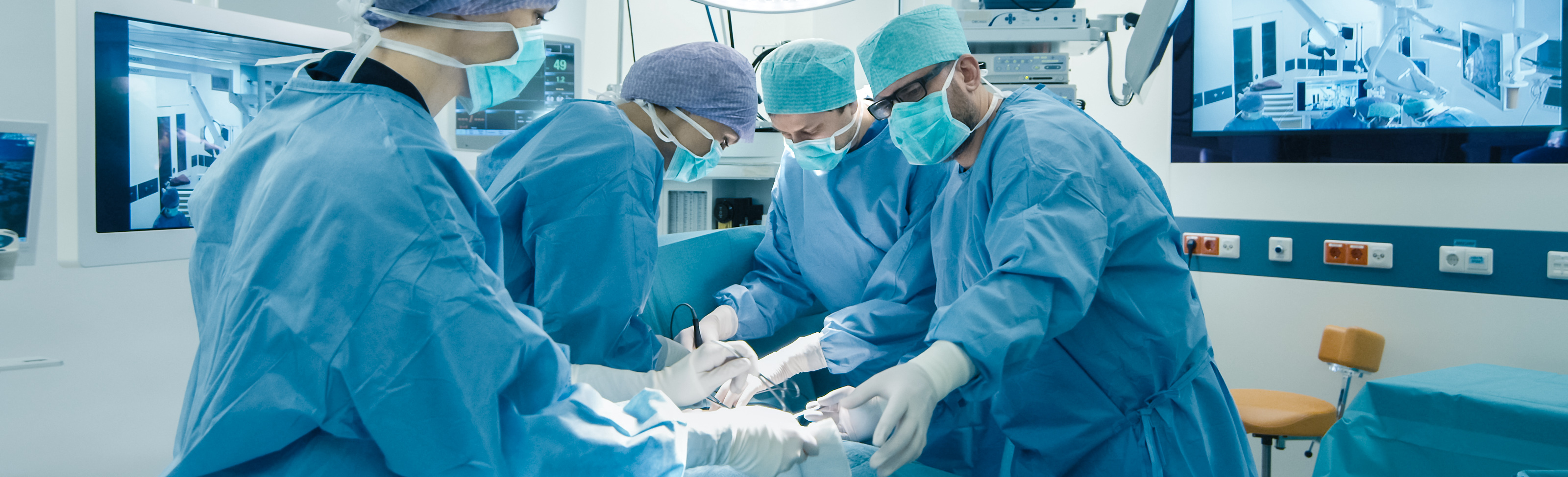 Four clinicians in blue surgical gowns in an operating room