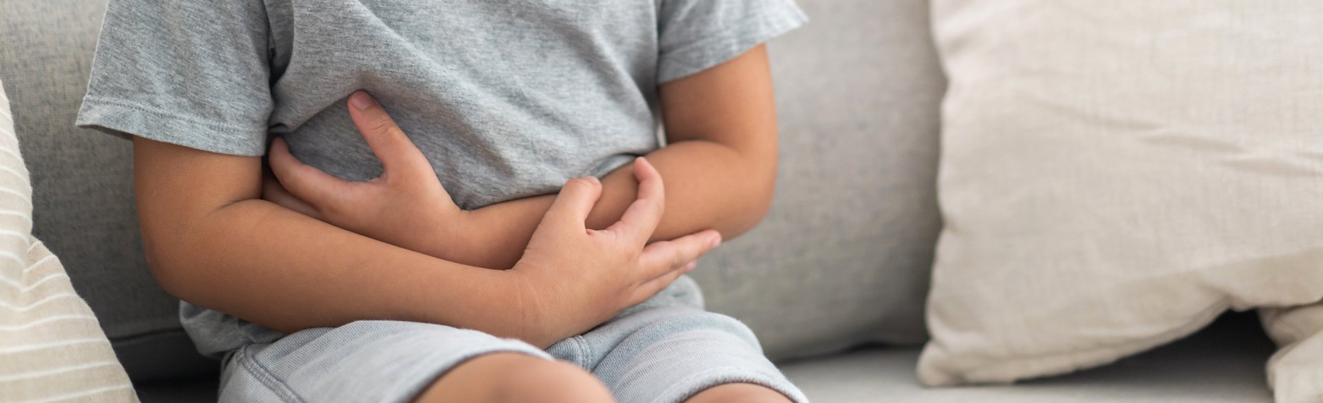Child sitting on a couch holding their stomach in pain