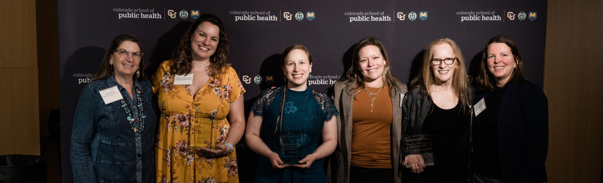 Six faculty and staff, two holding awards in front of step and repeat