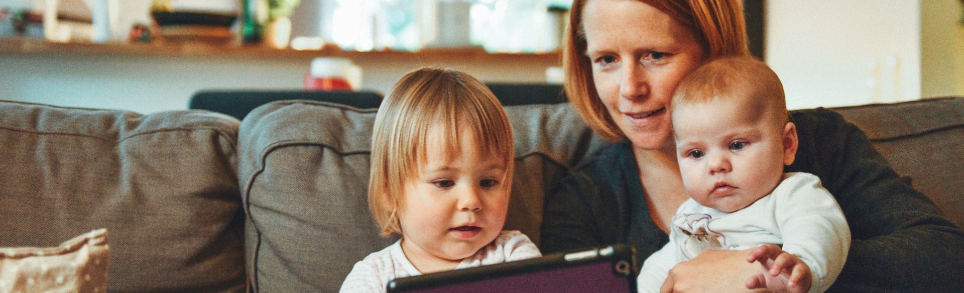 Mom sitting with 2 kids on couch looking at ipad