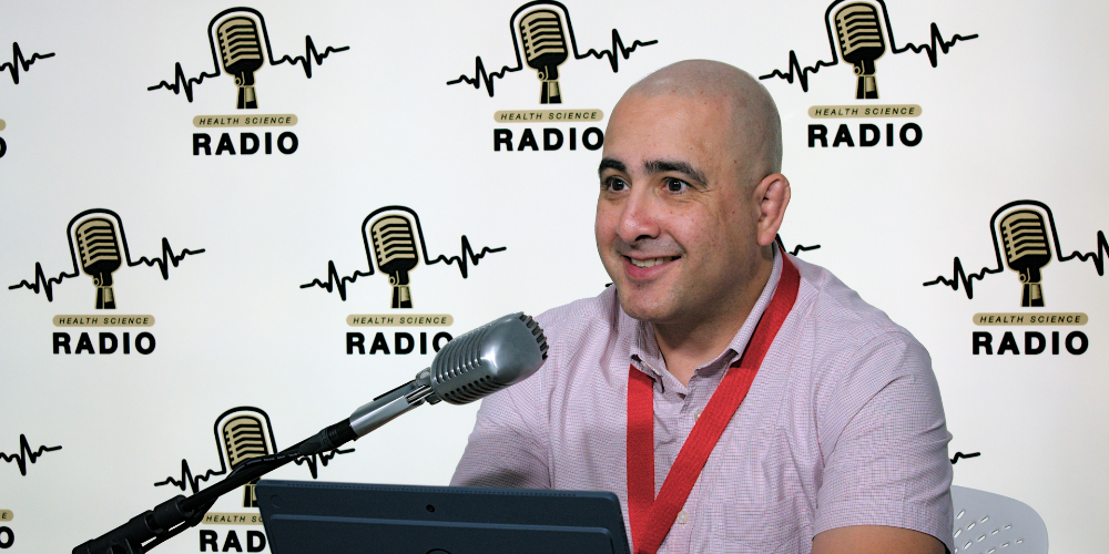 Daniel Goldberg, sitting in front of a microphone, is interviewed on Health Science Radio 