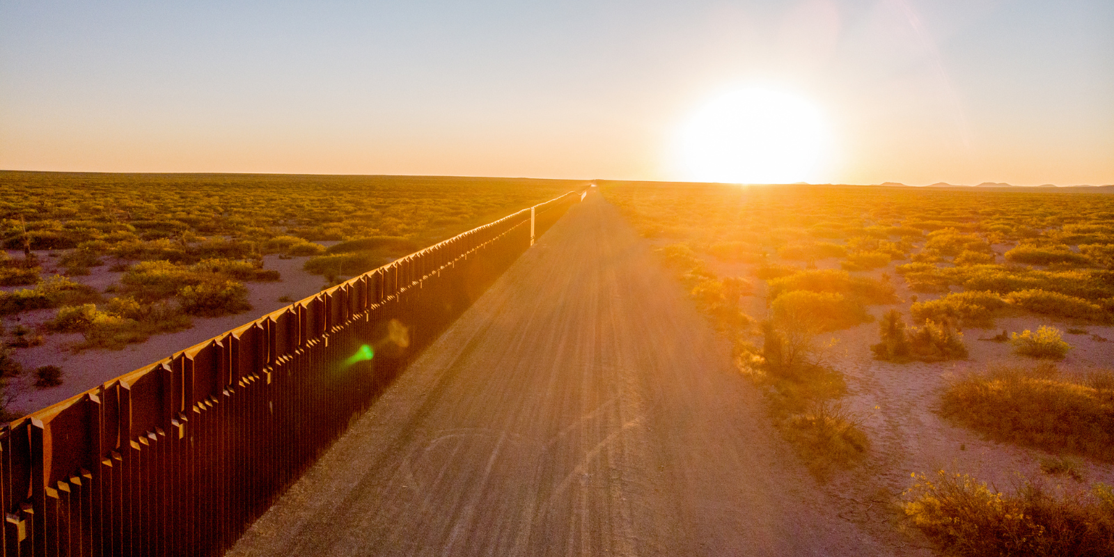 Image of a fence at the US southern border with the sun at the horizon.