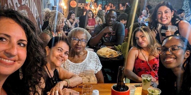 A group of students surround Mama Ruth at a small table in a cozy crowded bar