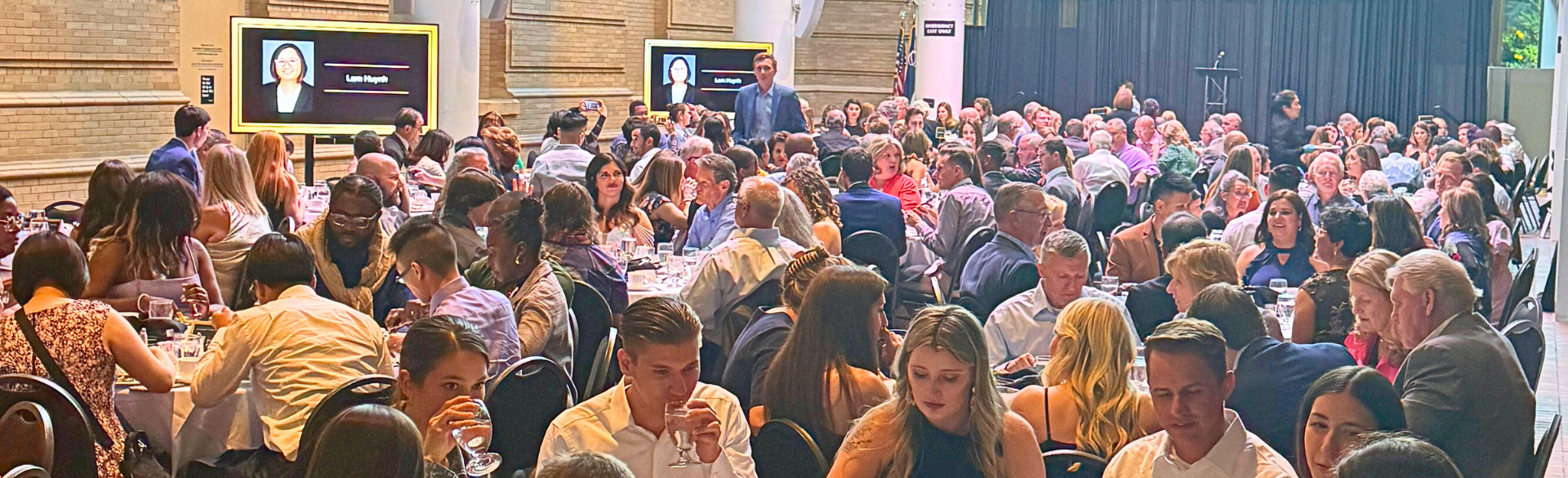large banquet hall with people seated at round tables eating and drinking