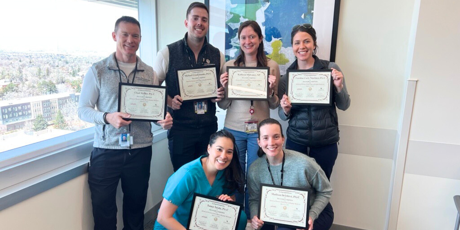 A group of advanced practice providers smile for a photo while holding their framed fellowship certificates.