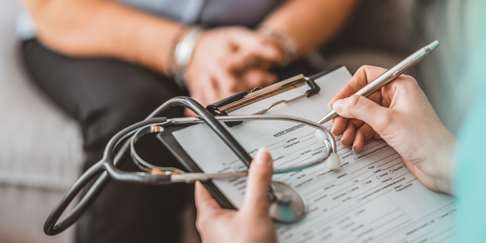 A doctor filling out a patient form as a patient sits in front of them.