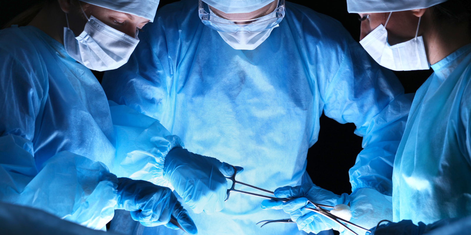 Three surgeons dressed in scrubs prepare for surgery.