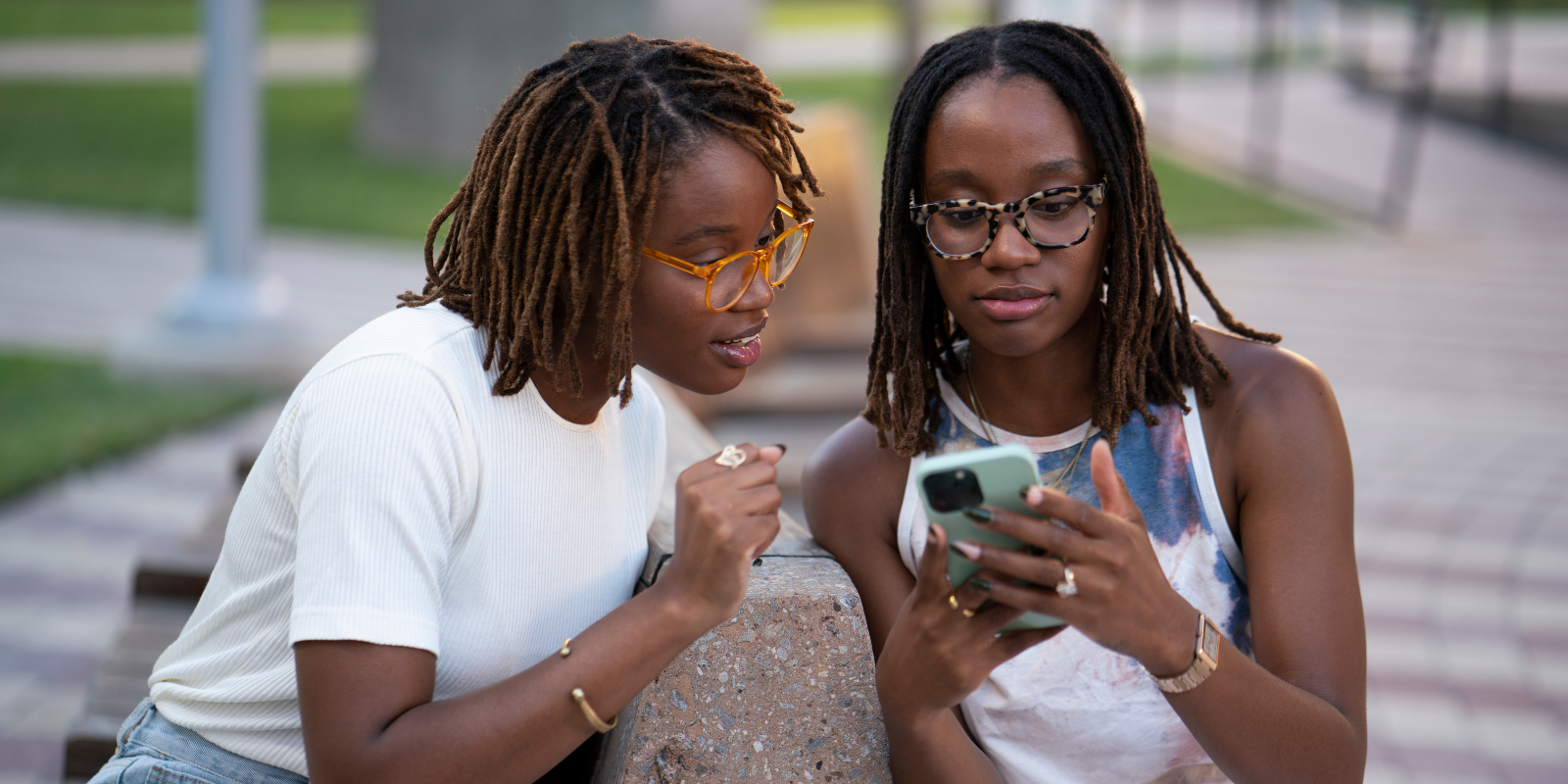 Two women sitting outside, looking at a phone screen. 