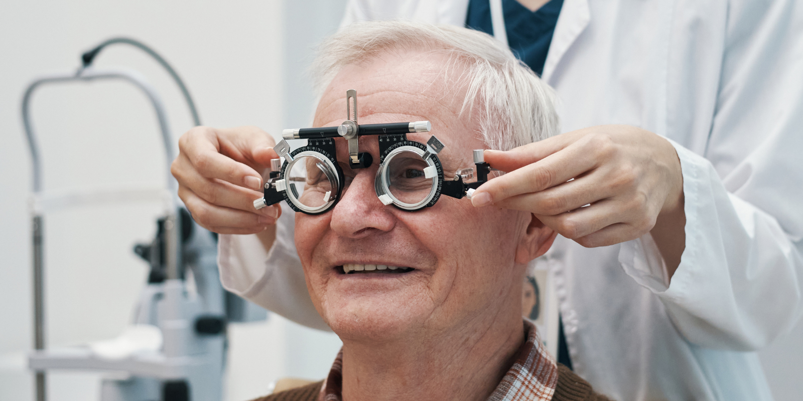 An older adult male patient smiles while getting an eye exam.