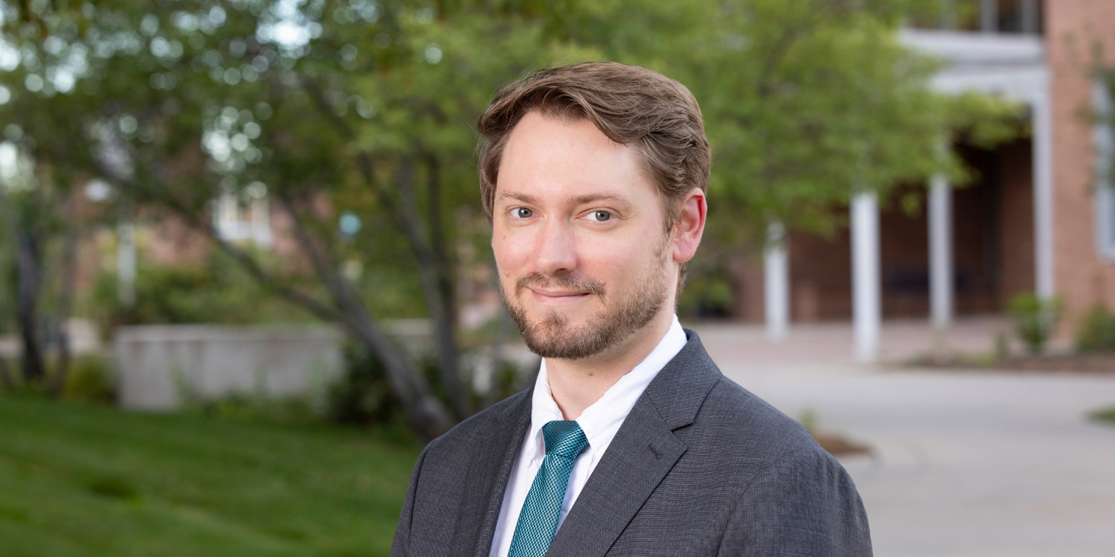 Riaz Qureshi, PhD, MS, dressed in a suit, smiles while standing outside at the CU Anschutz campus.