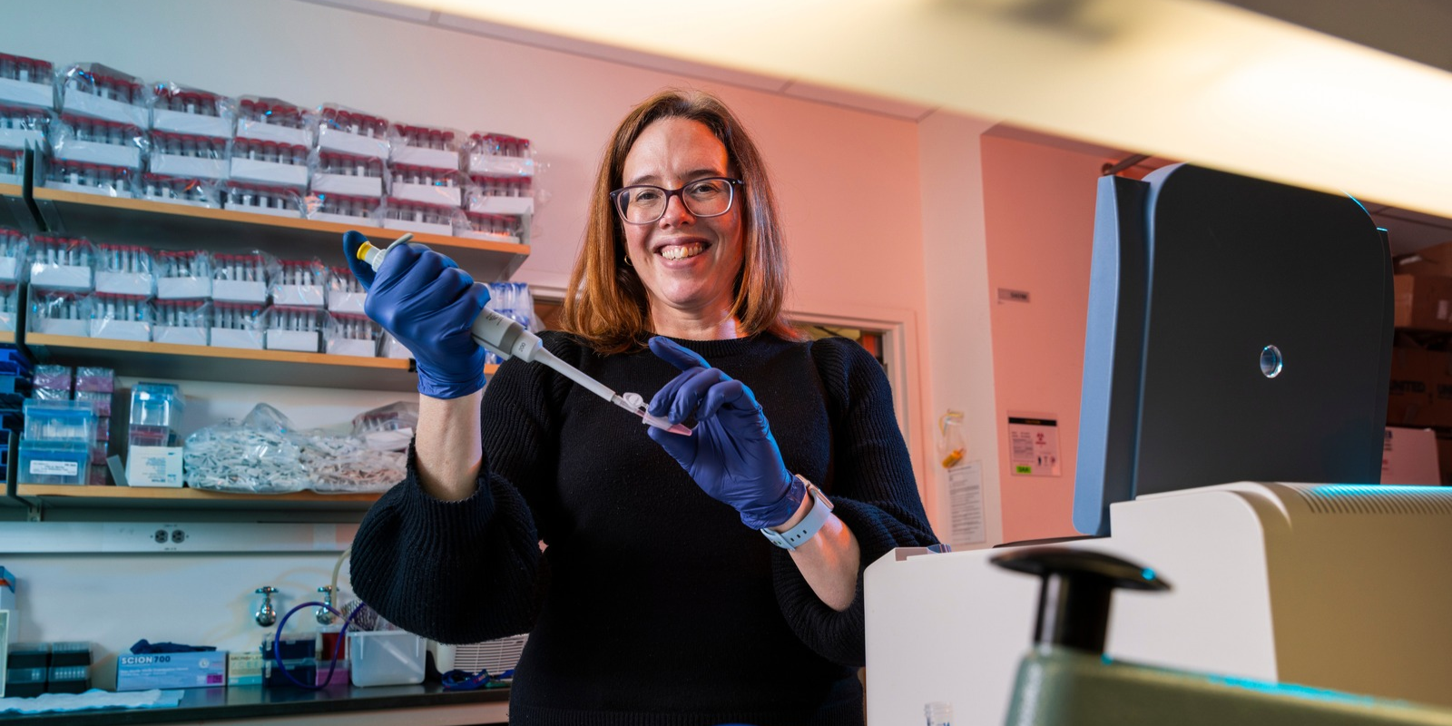 An ophthalmology researcher, wearing blue gloves and holding syringe, smiles while working in a lab.