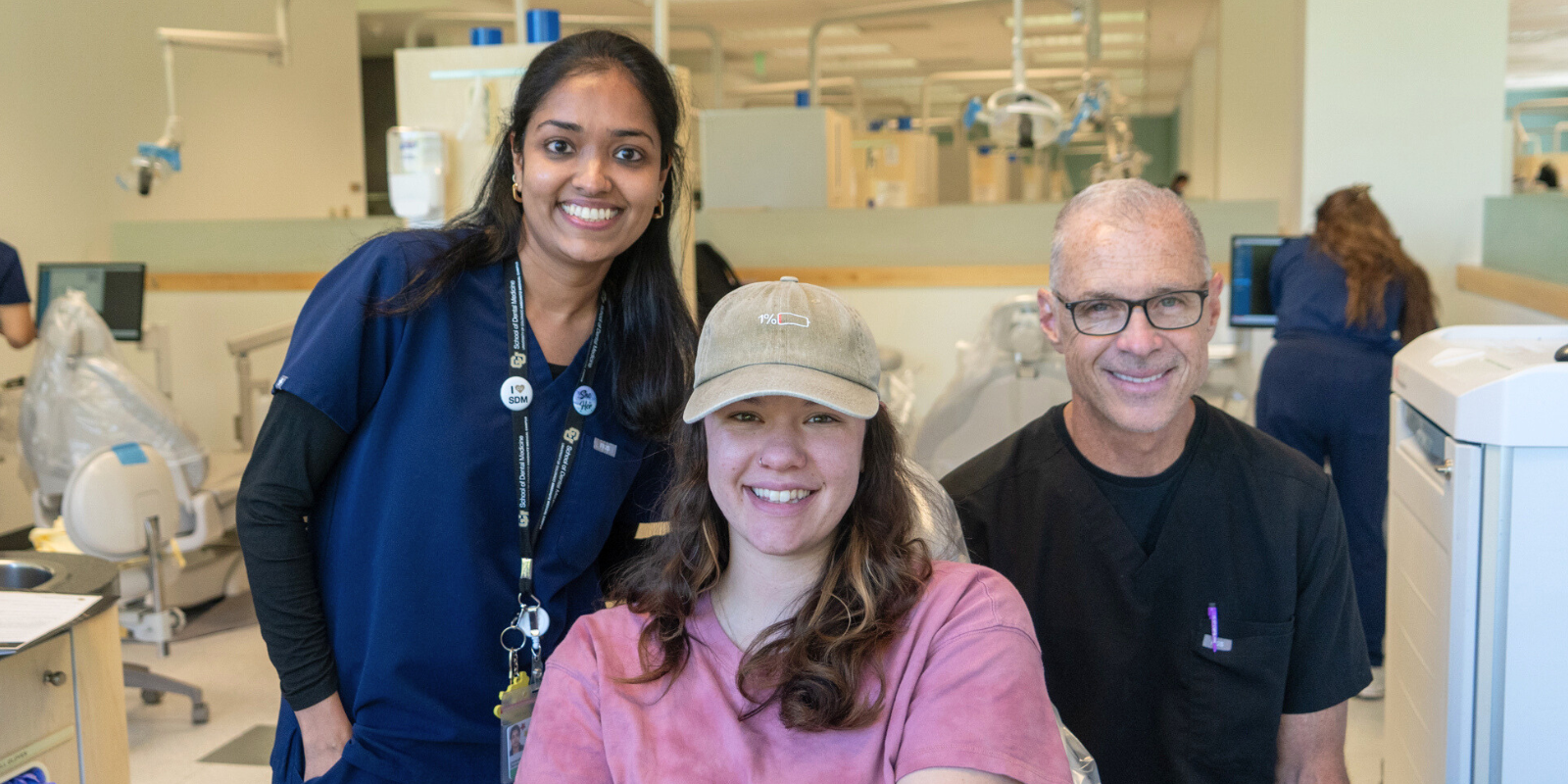 Dental student, patient, and faculty smiling together in the clinic