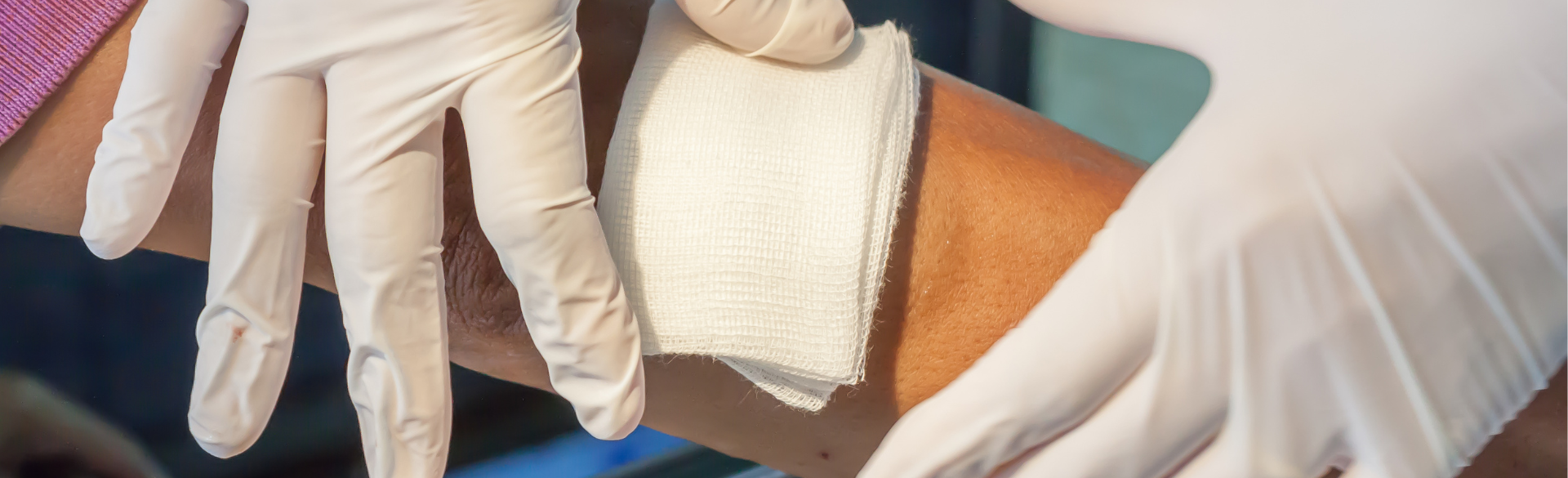 A close-up image of a health care worker's gloved hands applying a bandage to a wound