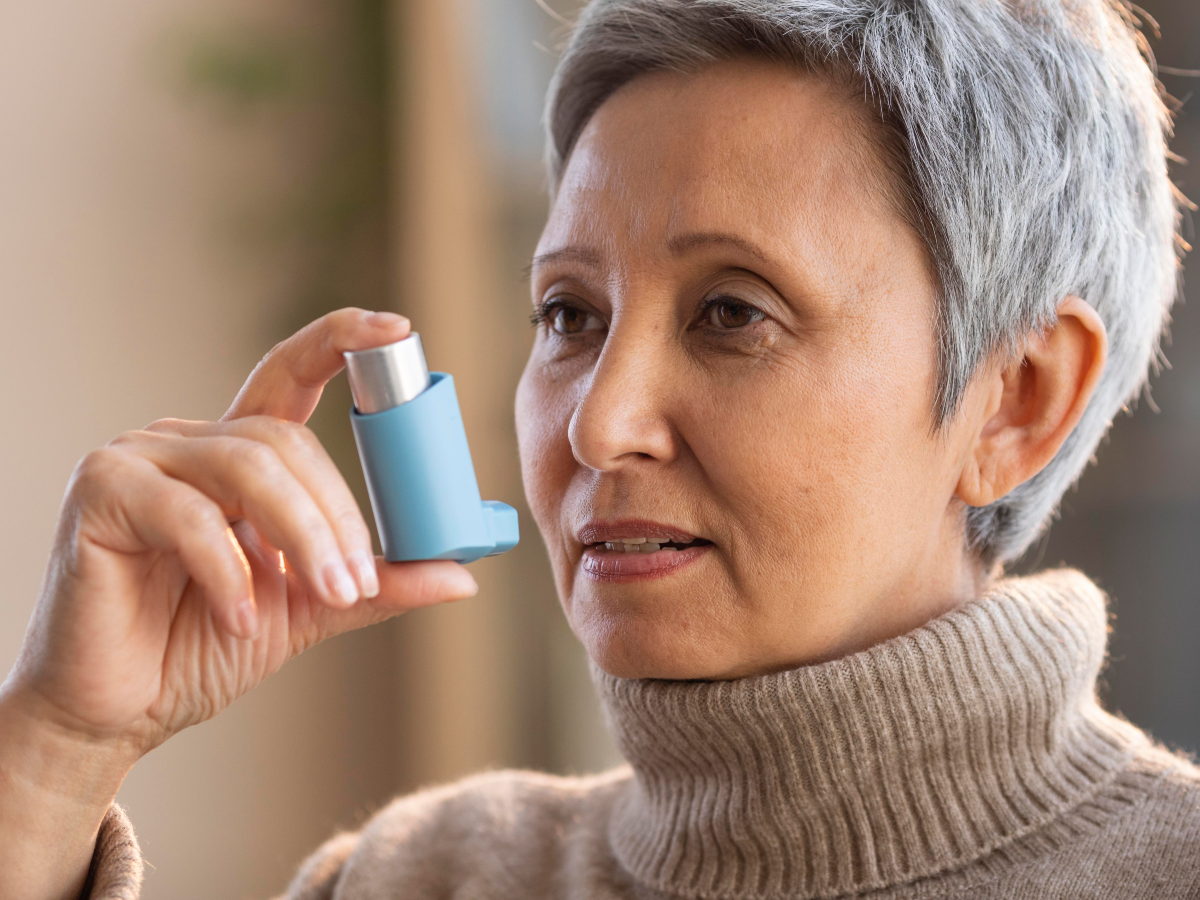 Image of elderly woman holding a inhaler near her face.