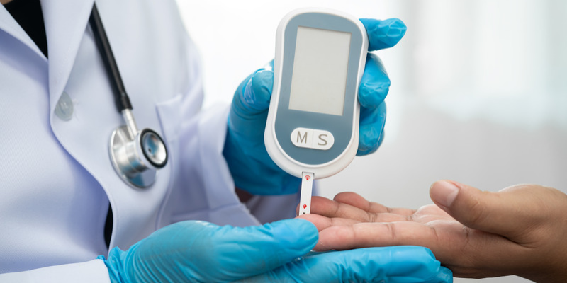 Dr. holding a blood glucose meter to a patient's hand.