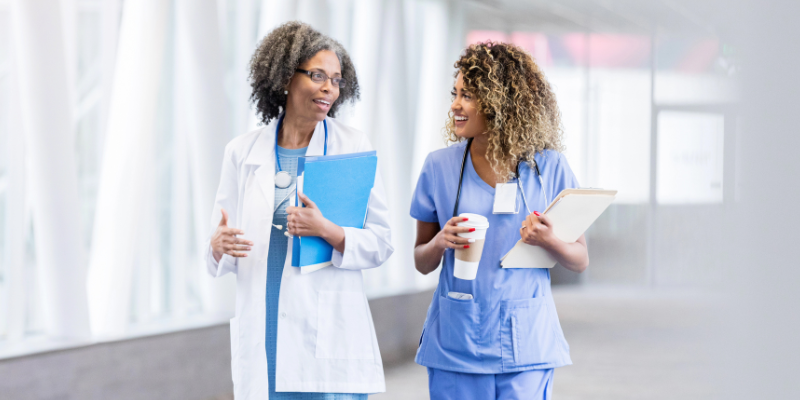Two female doctors walking down a hall talking to one another.