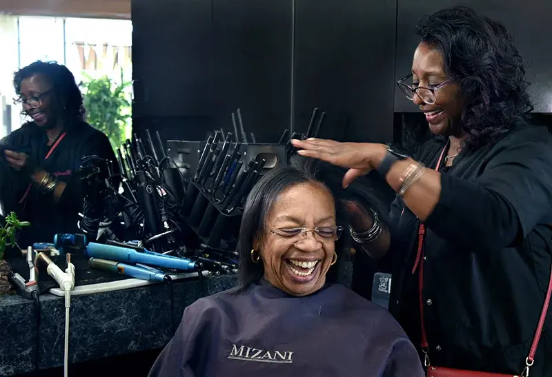 Two women laughing as one is styling the other's hair.