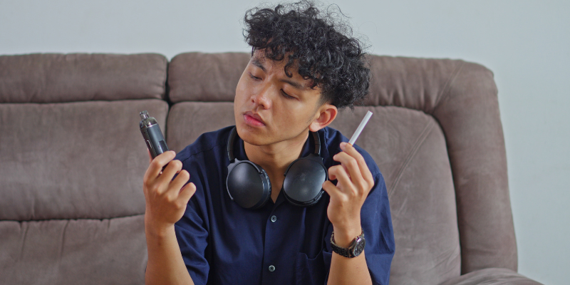 Perplexed teen holding a vape and cigarette in his hands.
