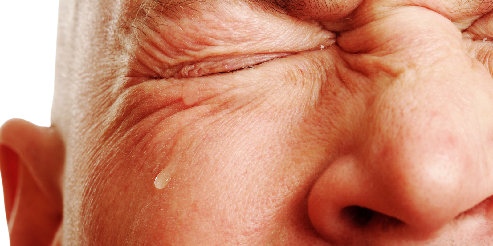 A close-up image of a man squinting from emotion. A tear rolls down his cheek. 