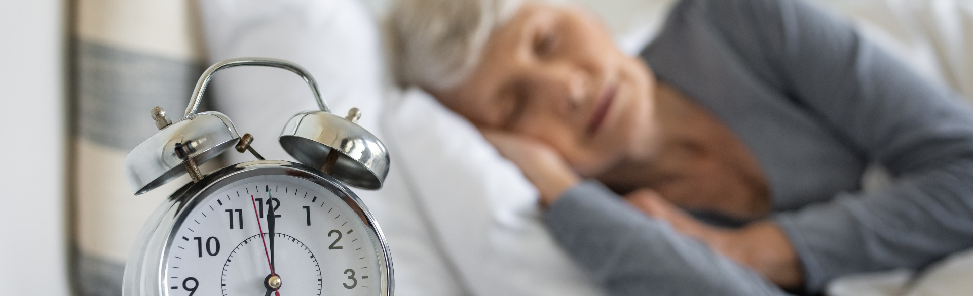 Elderly woman sleeping near an alarm clock that is set to 7 a.m. 