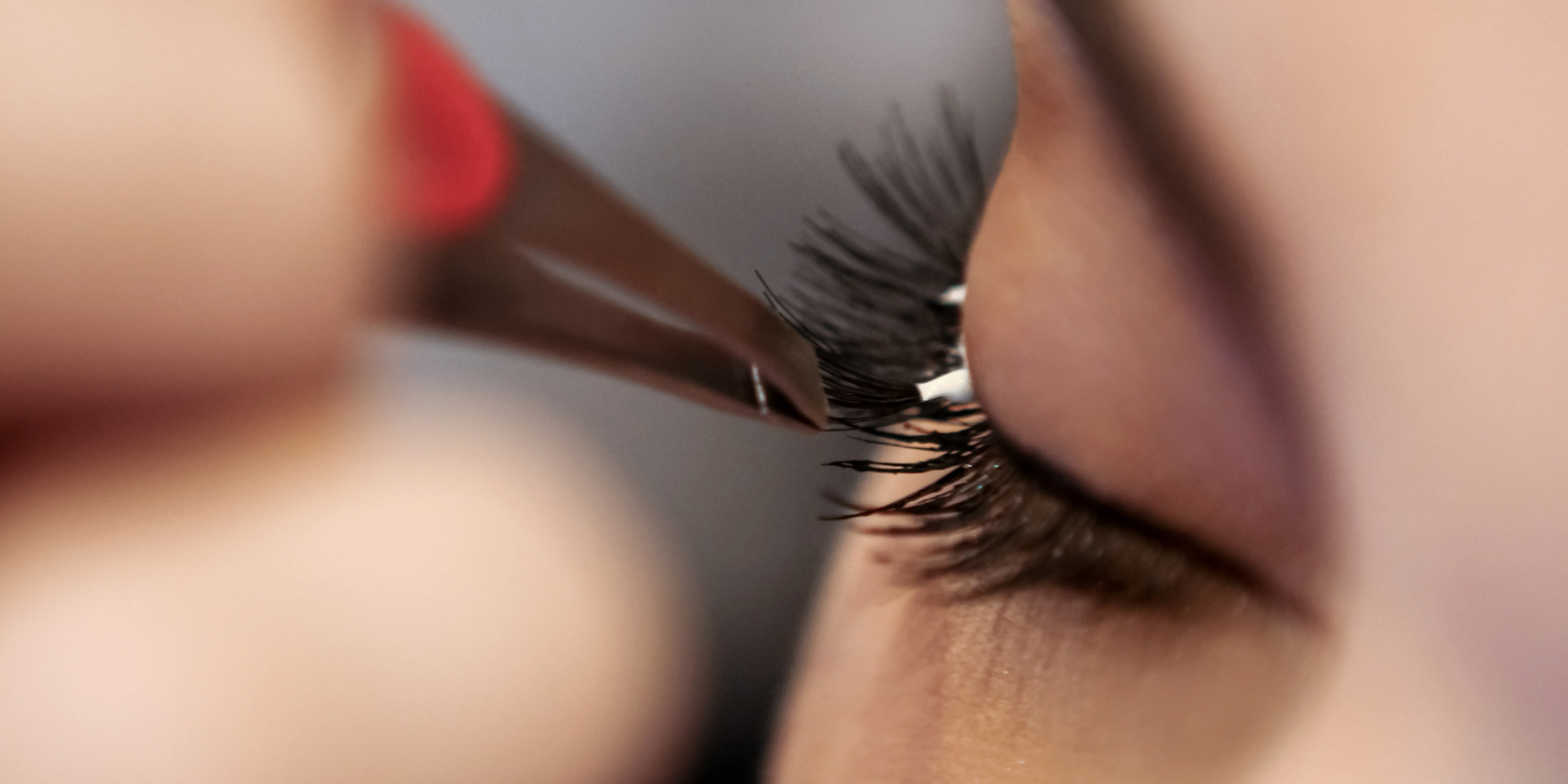 A close-up view of a woman applying fake eyelashes with tweezers