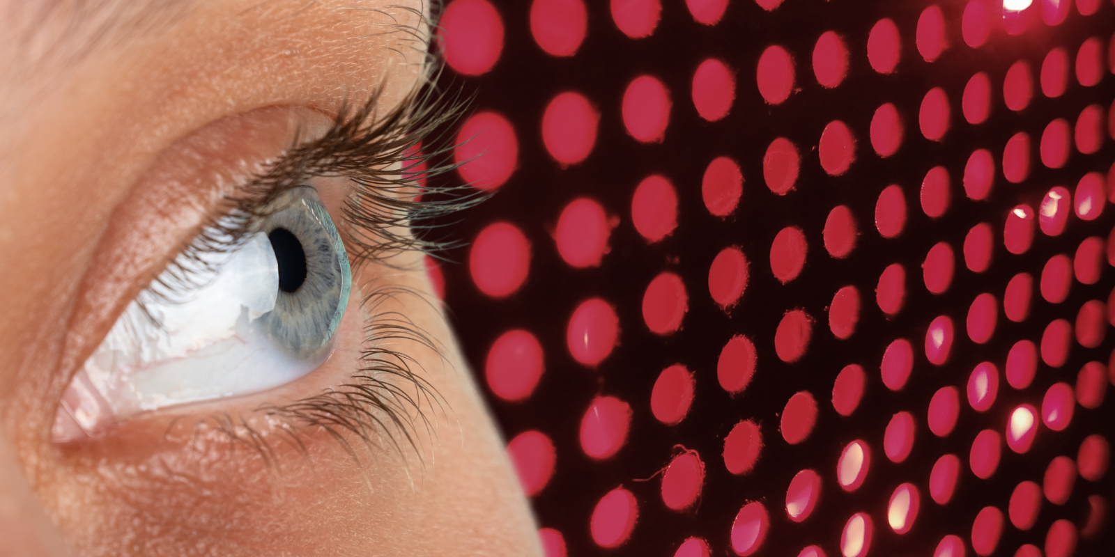 A woman's eye in the foreground with red LED lights in the background.