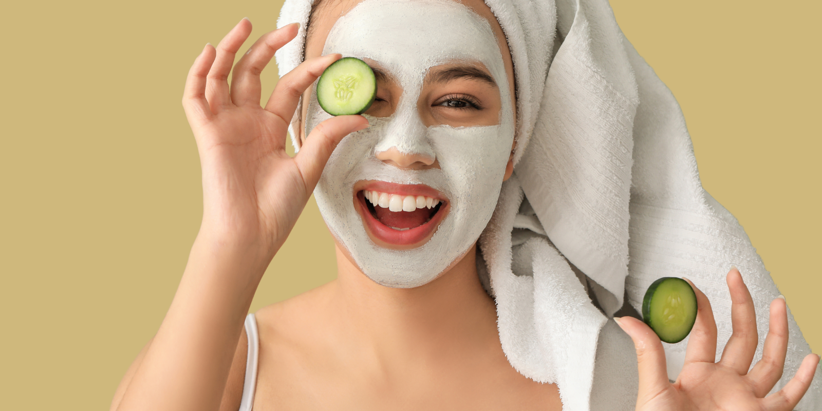 A woman in spa attire holds a cucumber up to her right eye. She is smiling.