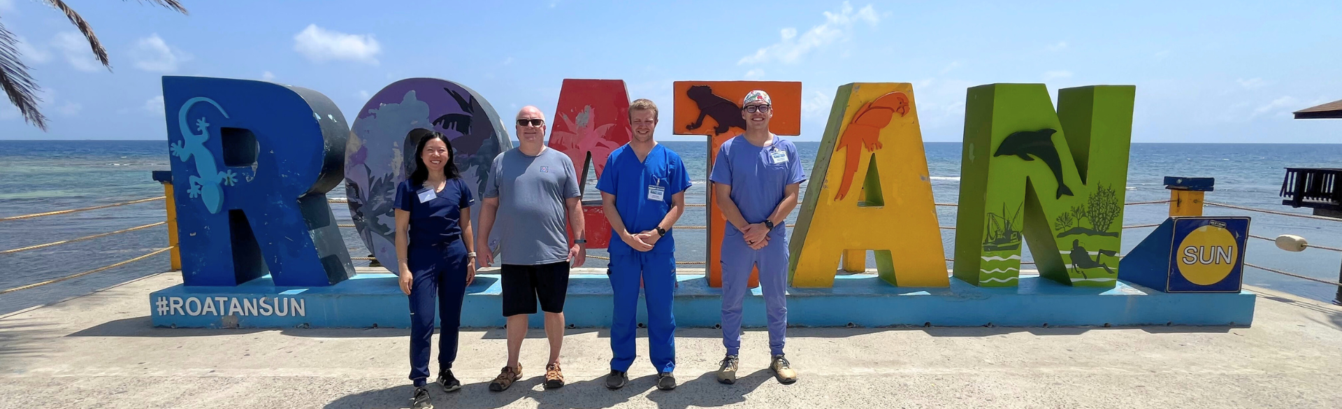 four people standing in front of large letters that spell ROATAN
