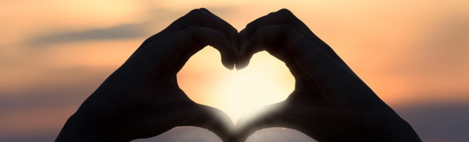 Image of hands making a heart shape with a yellow sky in the background. 