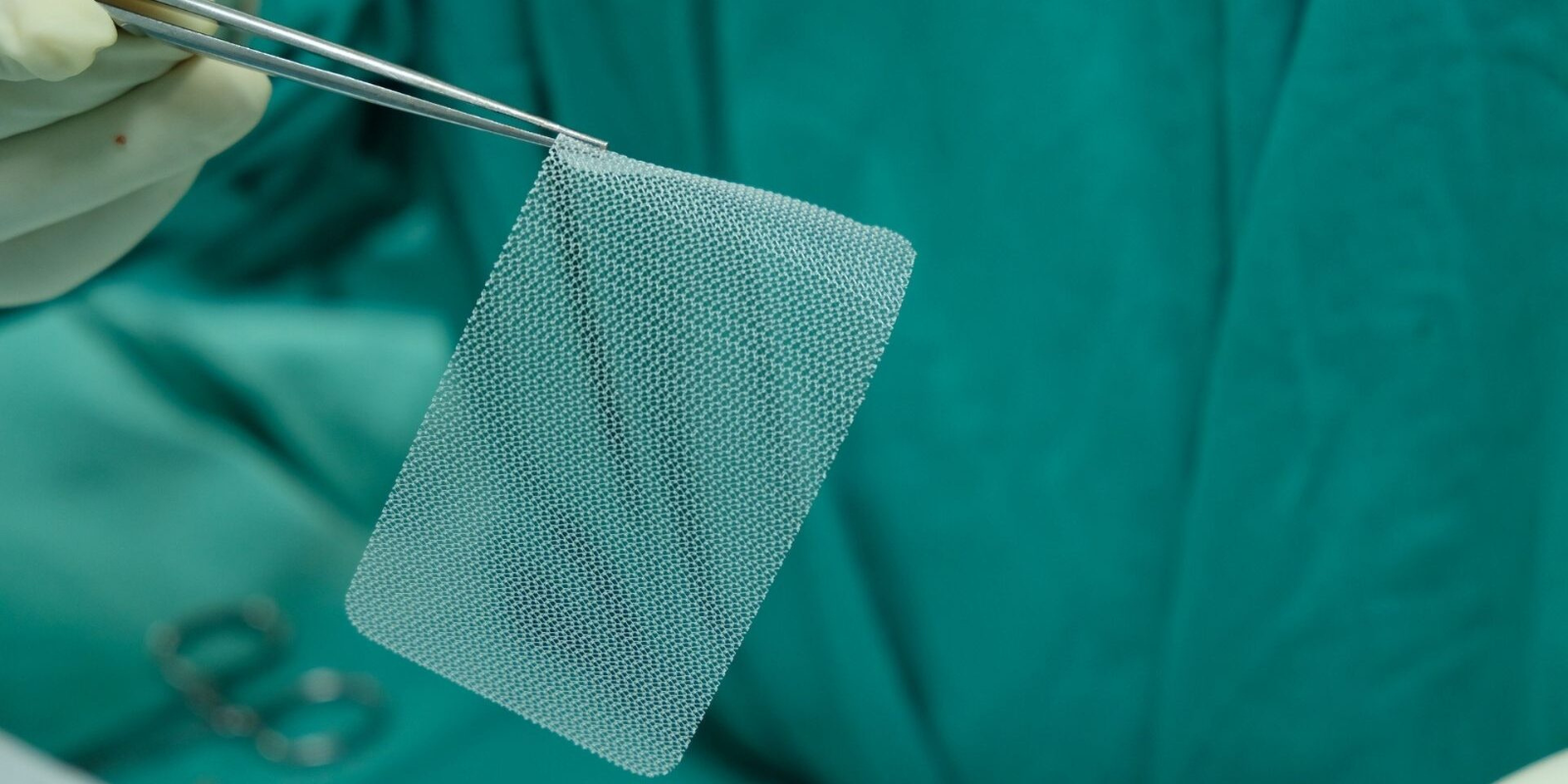 Surgeon using tweezers to hold a piece of surgical mesh