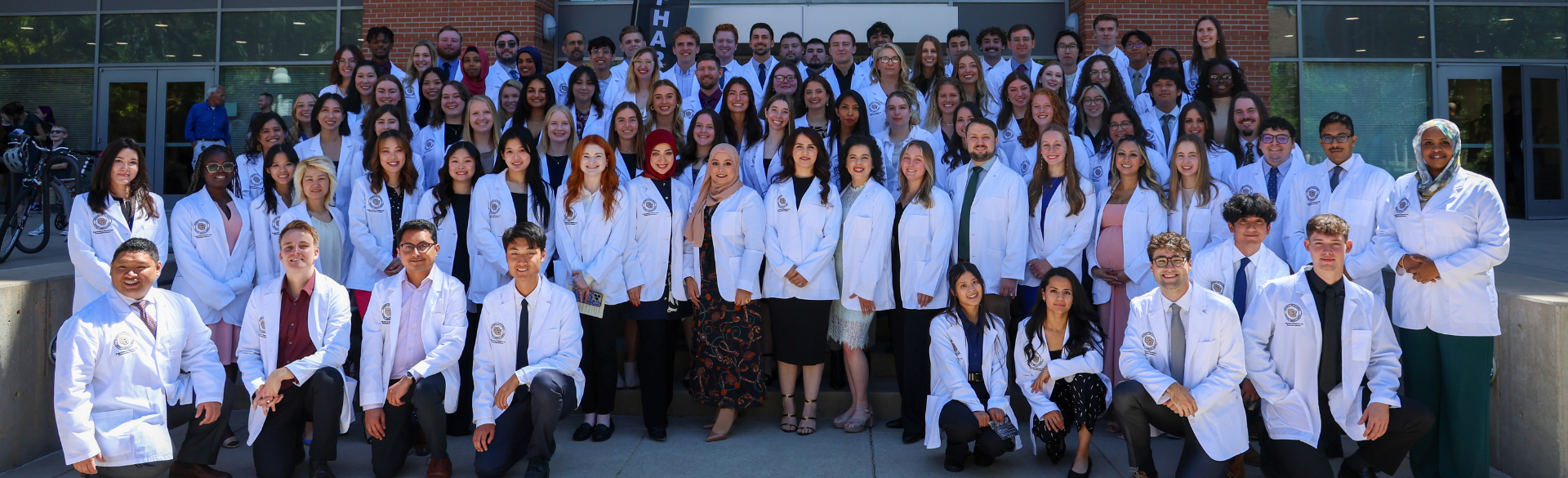 Ninety-six pharmacy students in their white coats gather in front of the school.