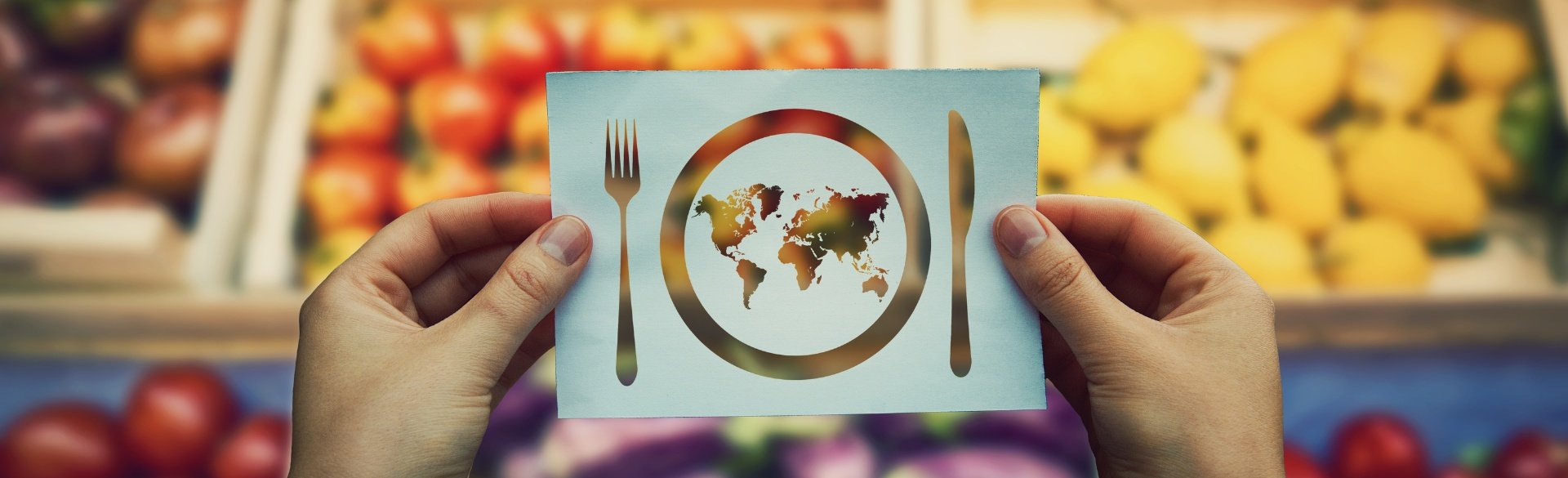 Person holding paper cut-out of fork, knife, and plate with the map of the world cut from inside