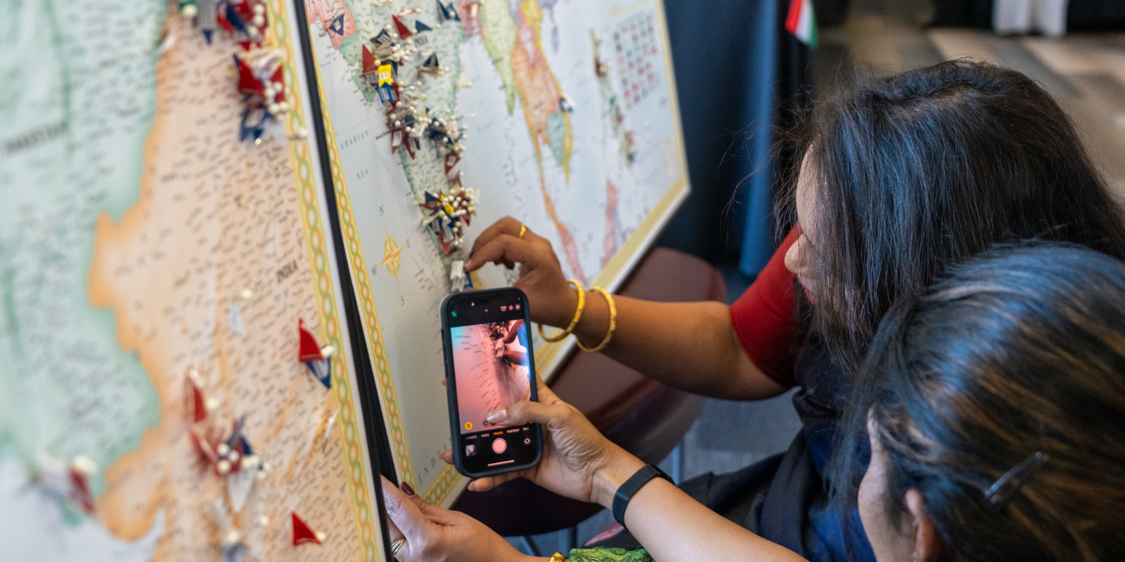 student pinning flag on world map with another student taking a photo