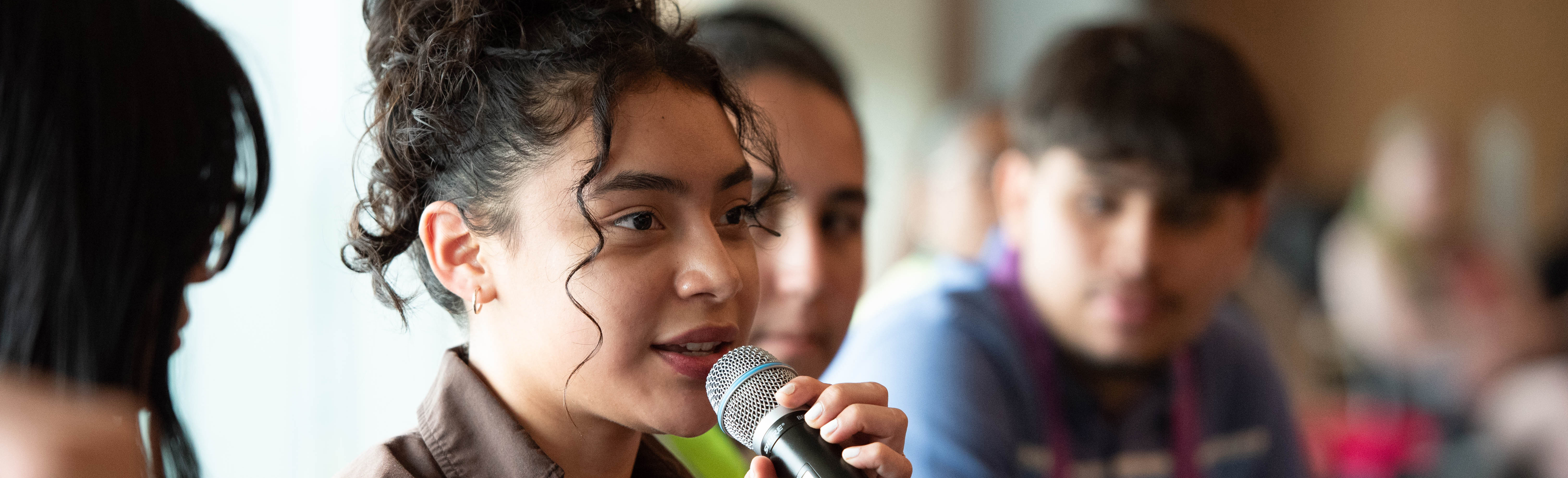 Young woman talks with microphone as others seated near her look on