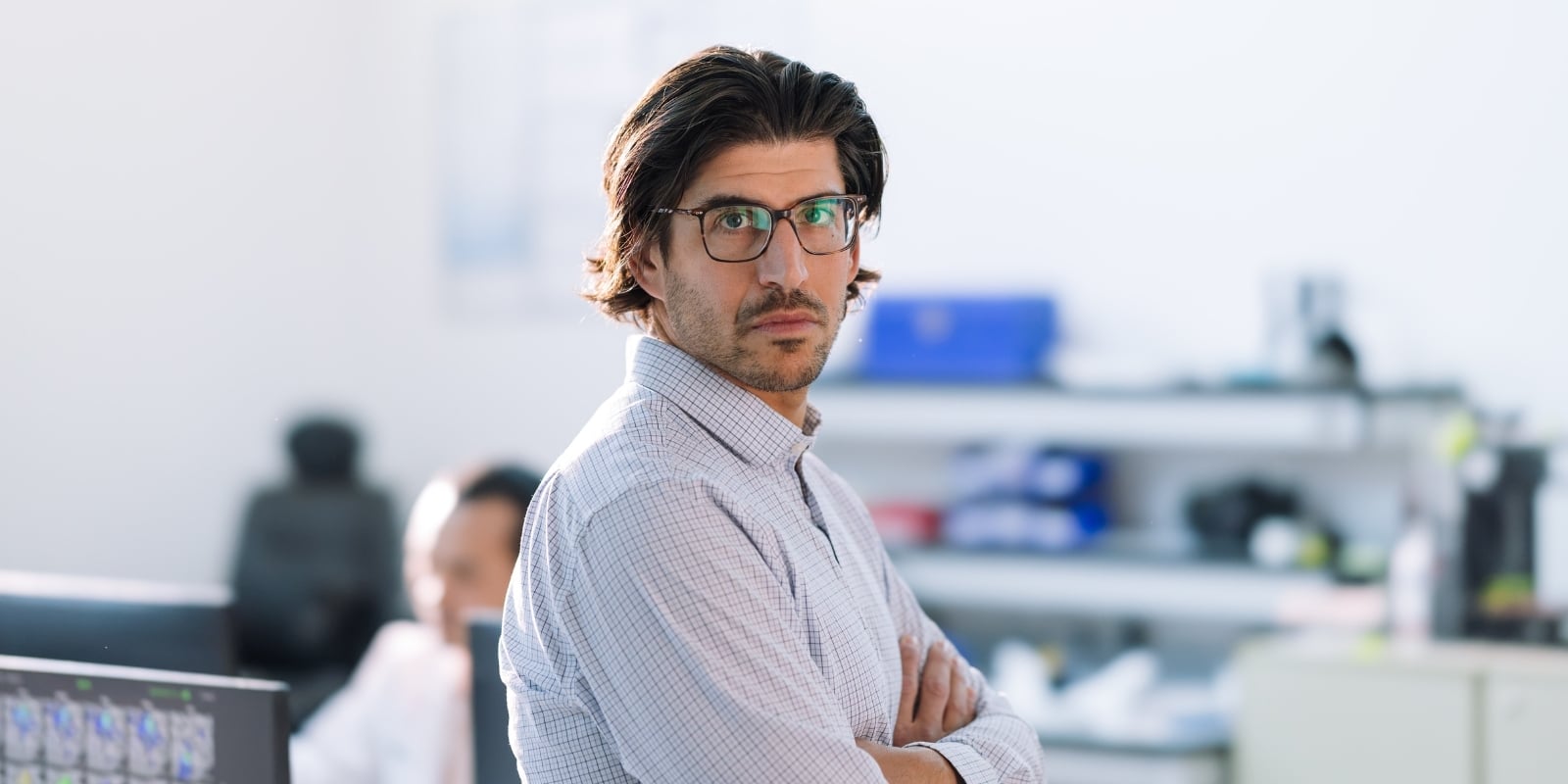 Daniel Kramer stands in a slightly out of focus laboratory, arms folded. 