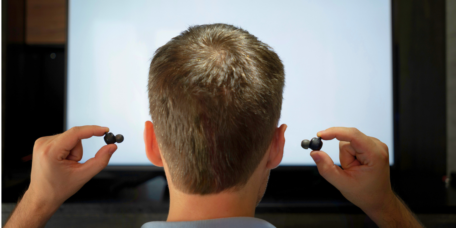 A photo illustration featuring a man at a movie theater putting in earplugs.