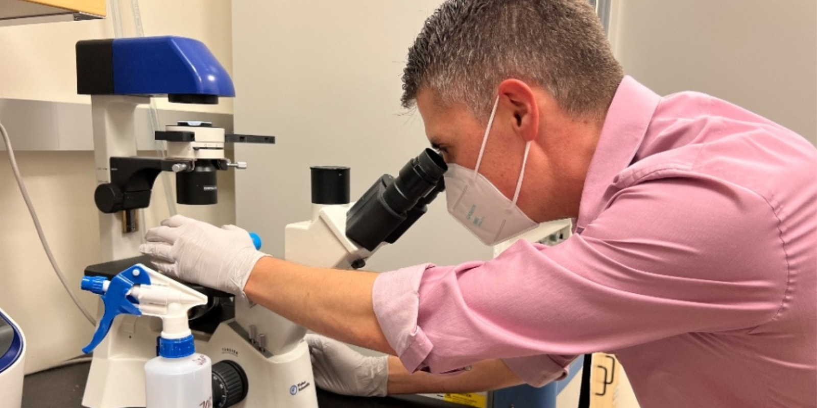 Matthew Sikora, PhD, looks into a microscope in a lab at the CU Anschutz Cancer Center.