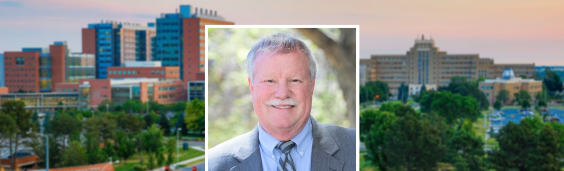 Man smiling in headshot wearing grey suit with blue shirt on a background of CU Anschutz Medical Campus