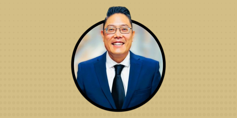 Dr. Brian Tsuji smiles in a blue suit with a gold background