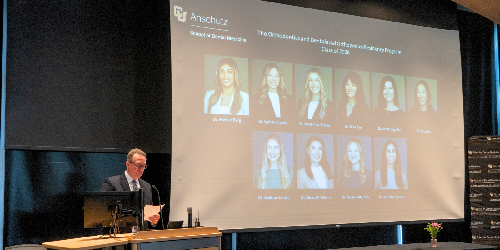 Dr Minick at podium with orthodontic residency class composite on screen