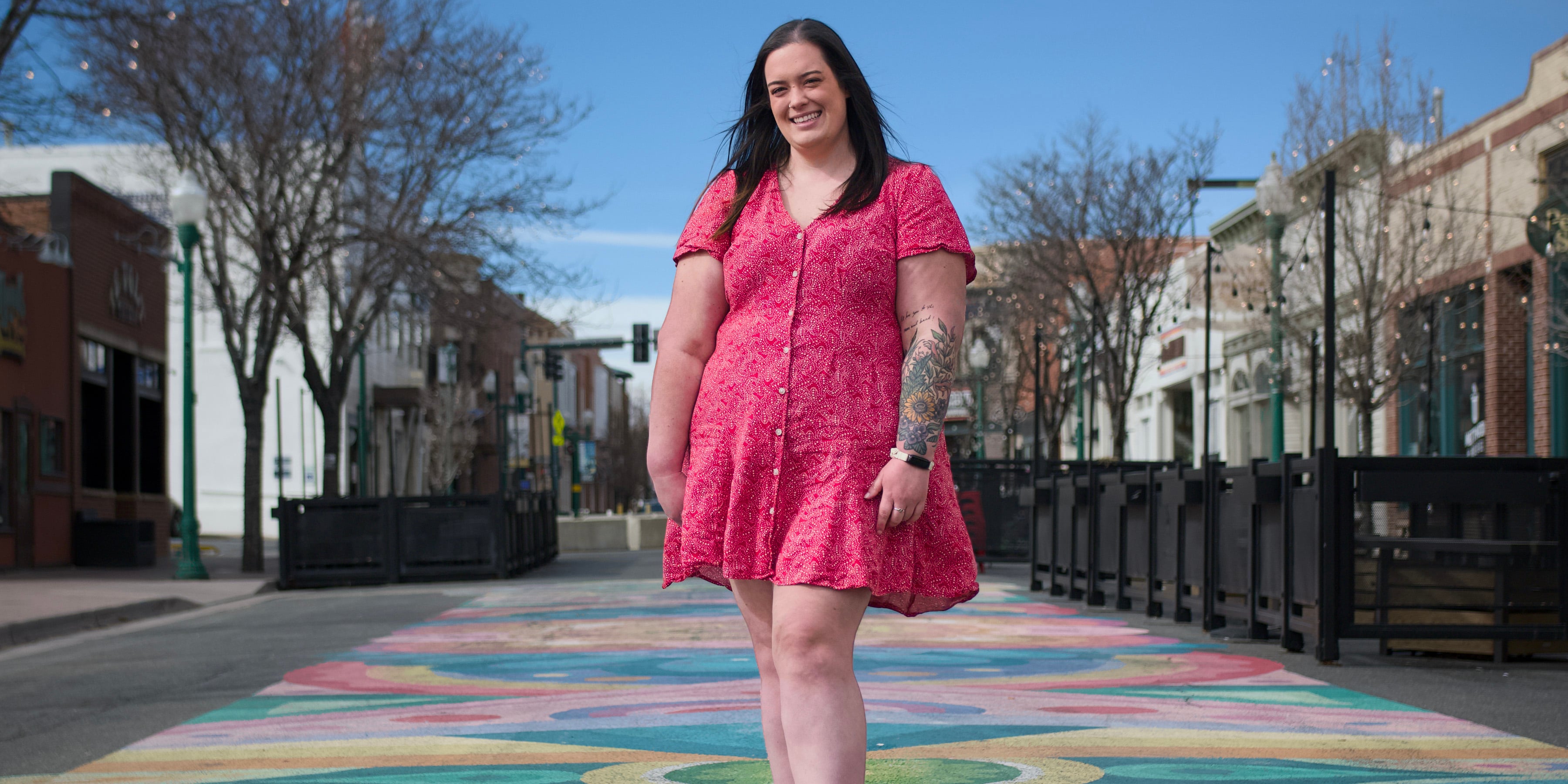 Hamilton poses standing on a colorful mural in downtown Arvada wearing a bright red dress