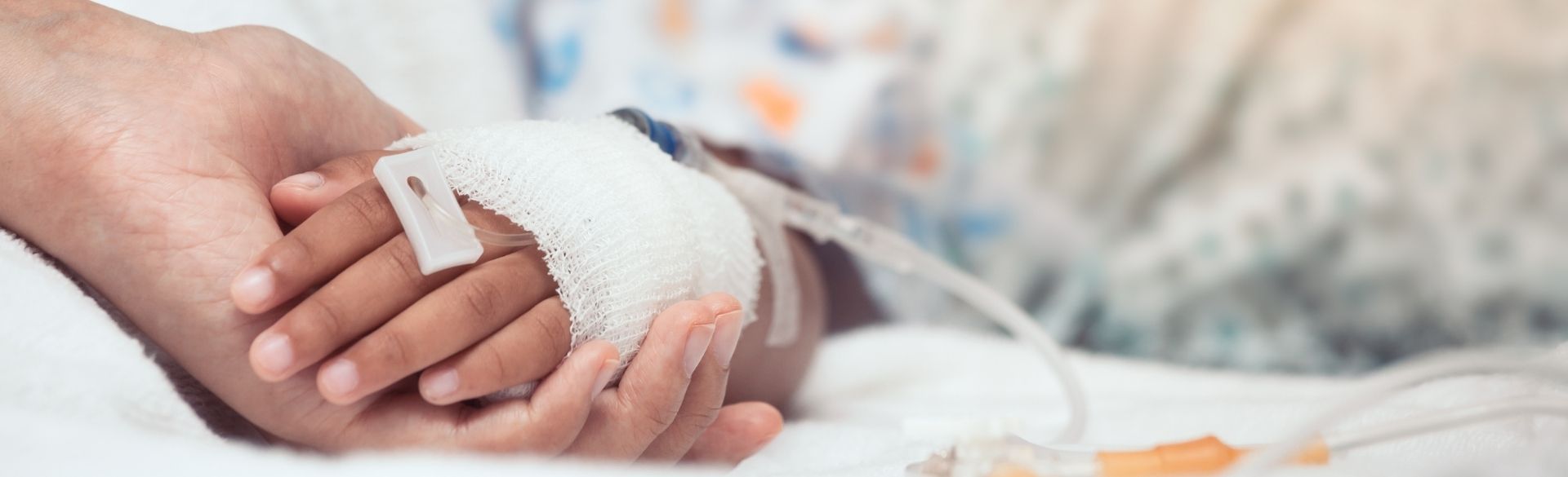 Caregiver hand holds child's gauze-wrapped hand with protruding IV tube