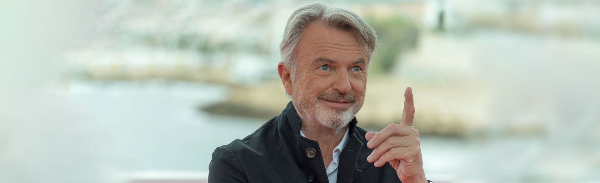 A grinning Sam Neill points toward the sky