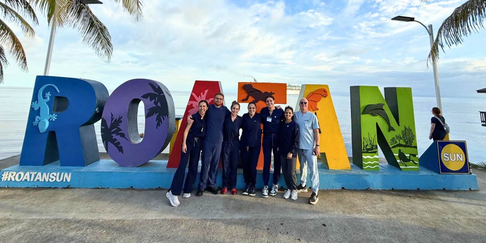 Group of dental students and faculty in front of Roatan sign at the beach in Honduras.