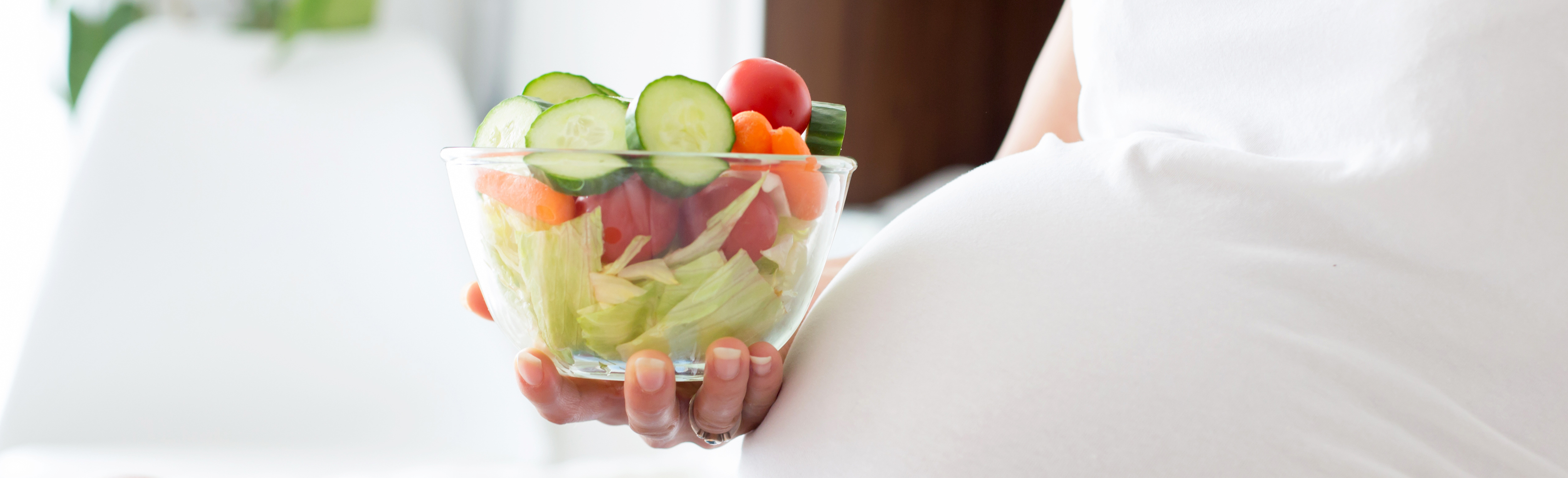 Pregnant woman in white shirt holding bowl of vegetables