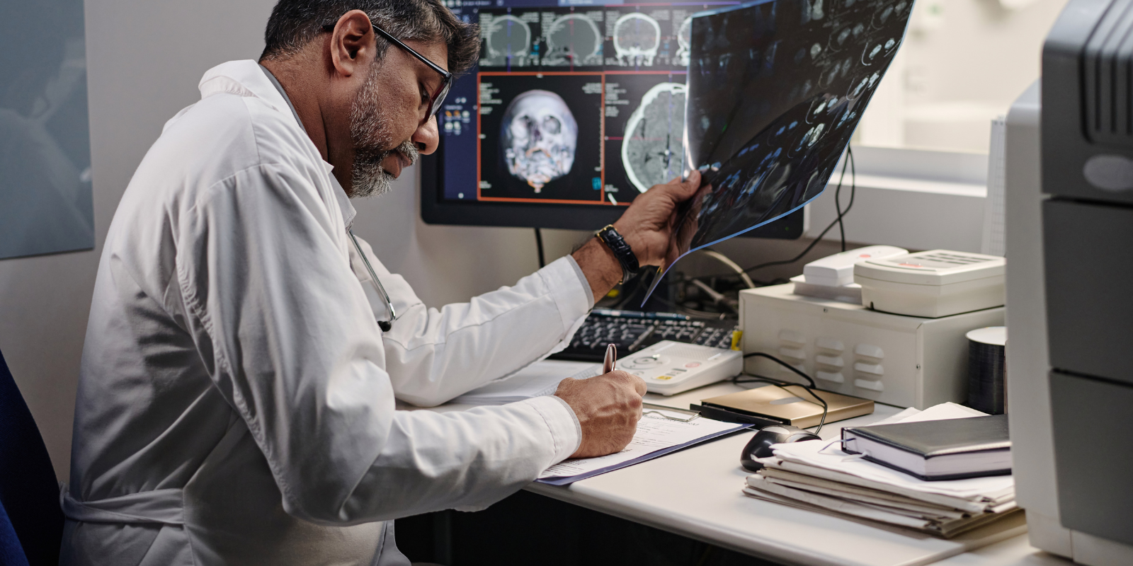 A radiologist studies a scan and takes notes at his computer.