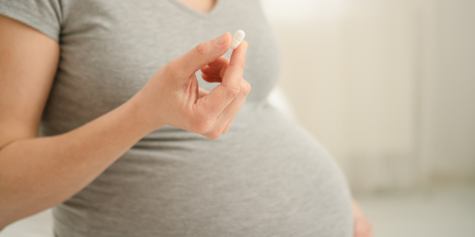 Photo of pregnant woman holding a white pain reliever pill. 