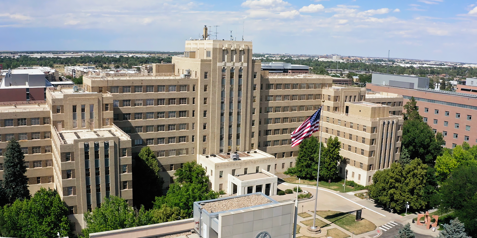 Fitzsimons Building on a partly cloudy day. A flag flies in front of the building.