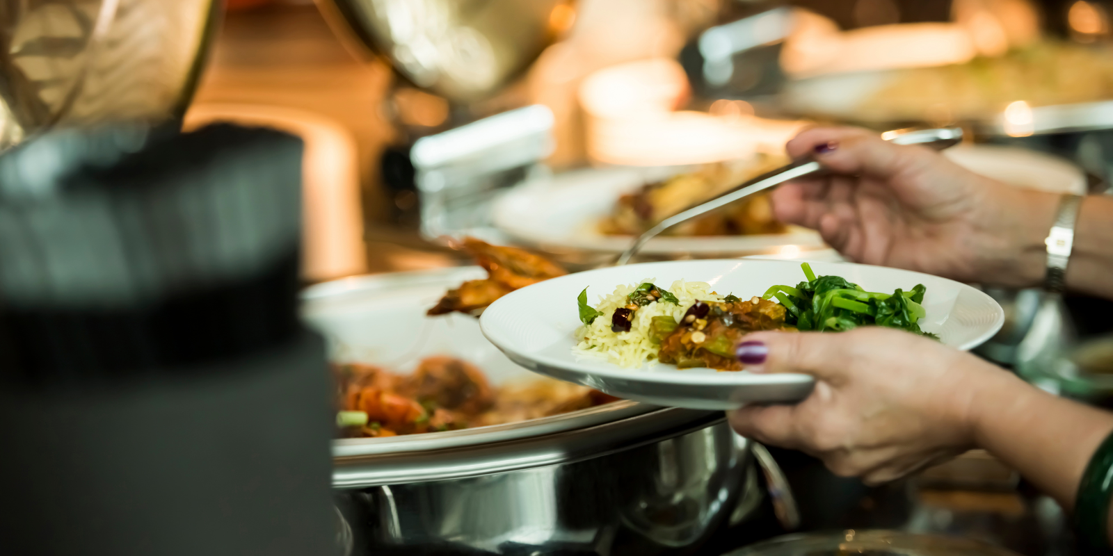 Unidentifiable woman serves herself a plate at a buffet. 