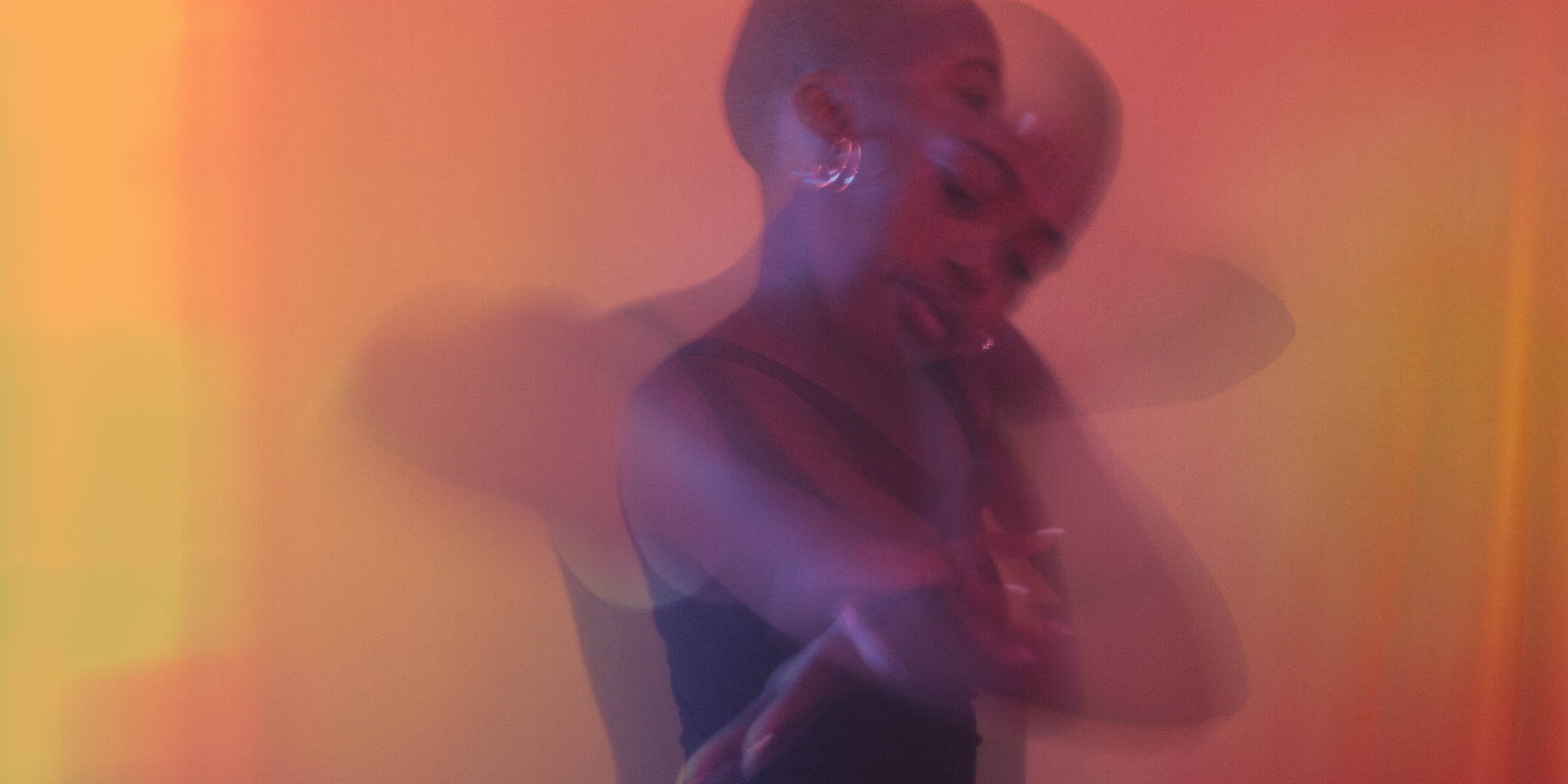 Image shows a woman with short hair moving around, possibly dancing, in purple and orange light. 